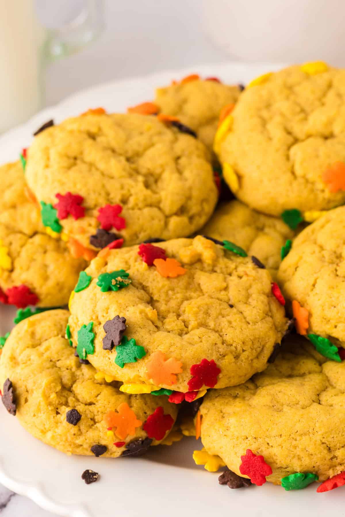 a pile of pumpkin cookies with autumn sprinkles on a round white plate.