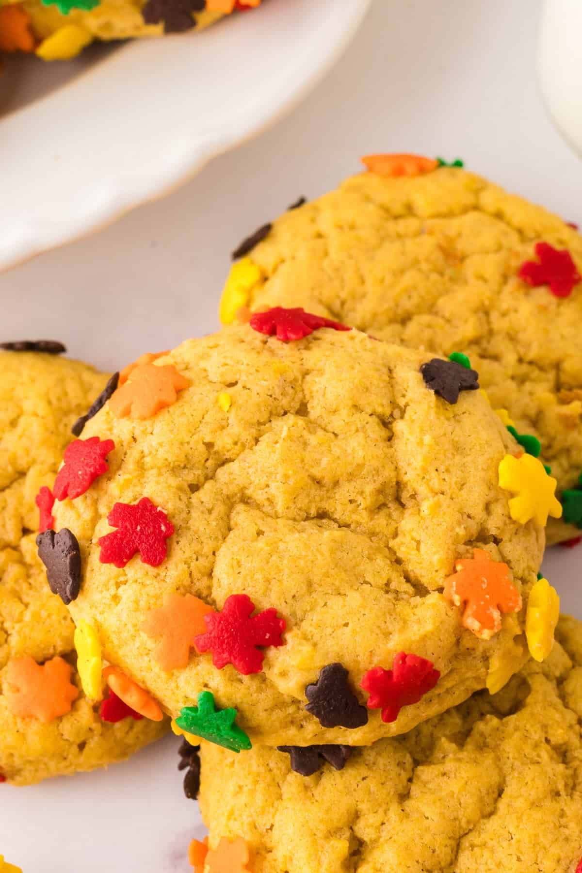 a pile of pumpkin cookies with autumn sprinkles on a marble counter.