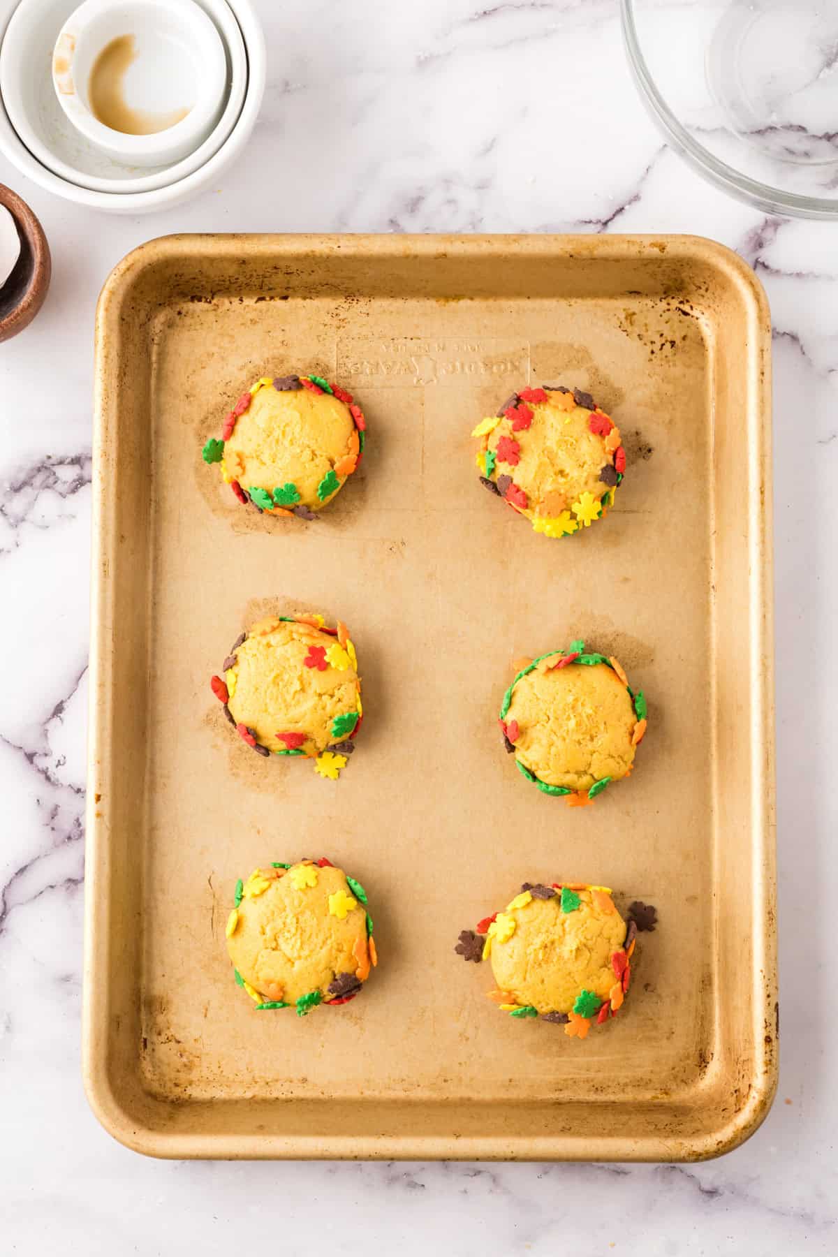 six pumpkin cookie batter balls on a baking sheet.