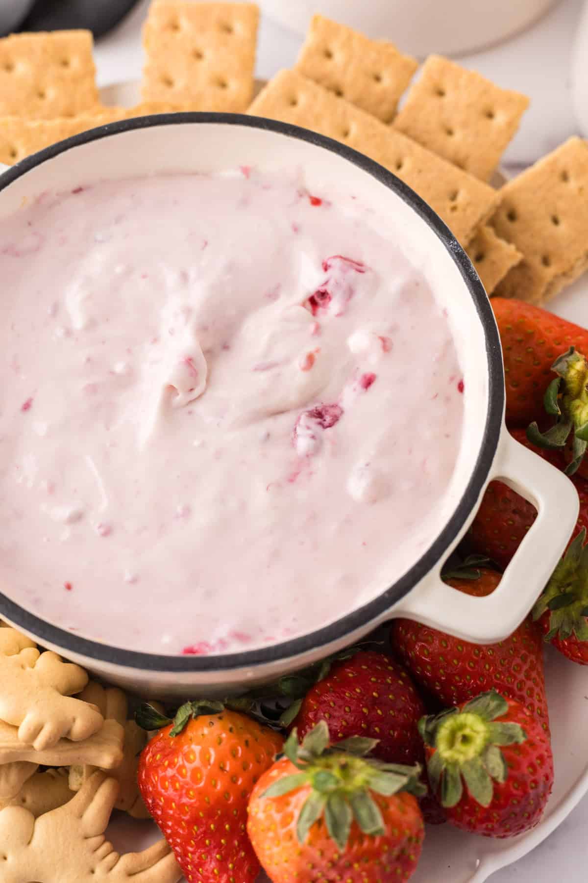 small bowl with crackers around it with the raspberry cheesecake dip recipe inside.