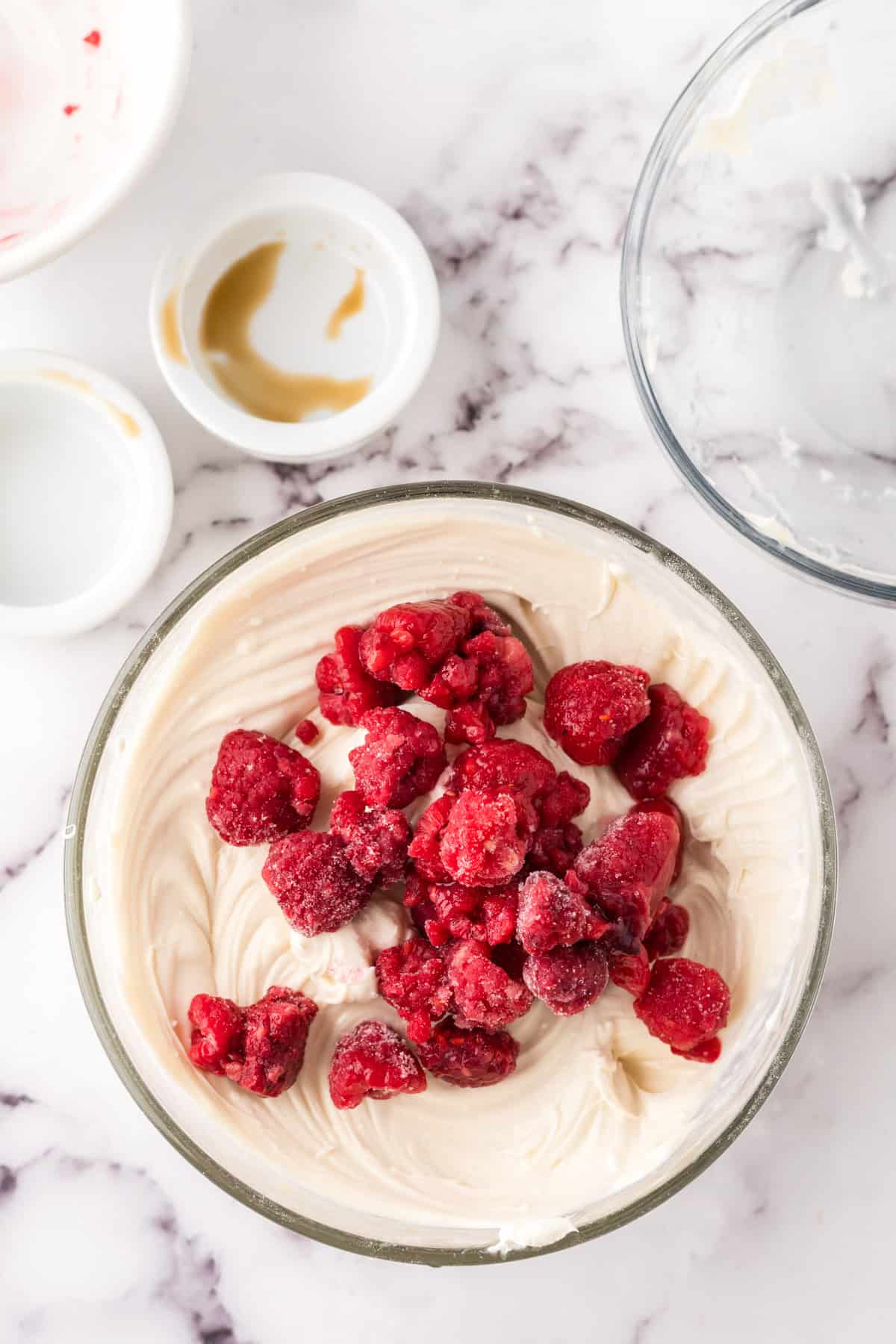 clear mixing bowl in the process of making raspberry cheesecake dip with fresh raspberries on top.