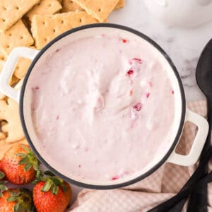 small bowl with crackers and berries around it with the raspberry cheesecake dip recipe inside.