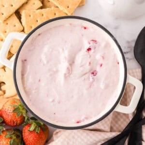 small bowl with crackers and berries around it with the raspberry cheesecake dip recipe inside.