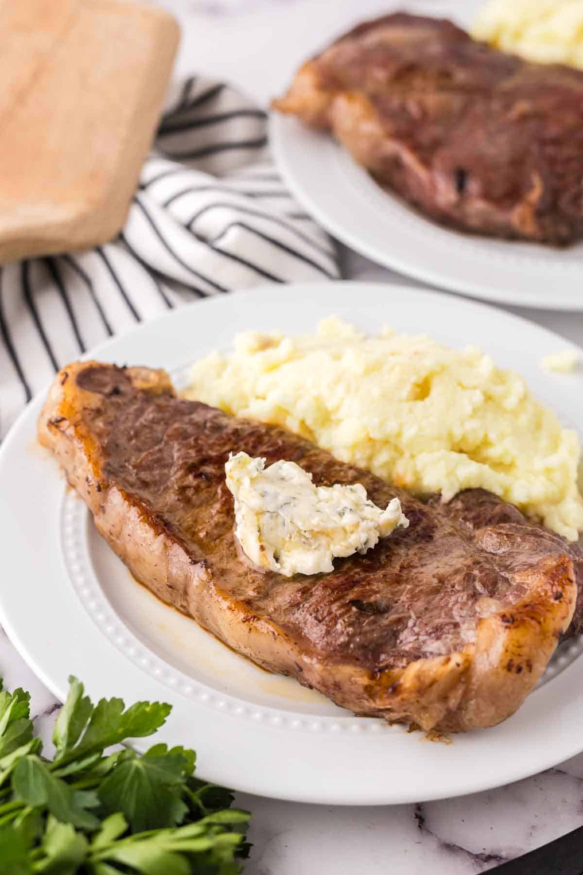 a steak dinner on a white plate with mashed potatoes on the side with compound butter on top.