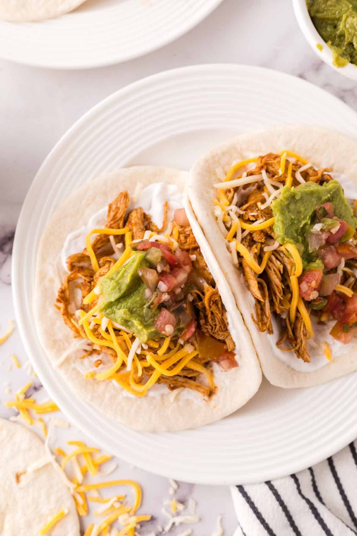 two shredded chicken tacos recipe on a round white plate with guacamole on top.
