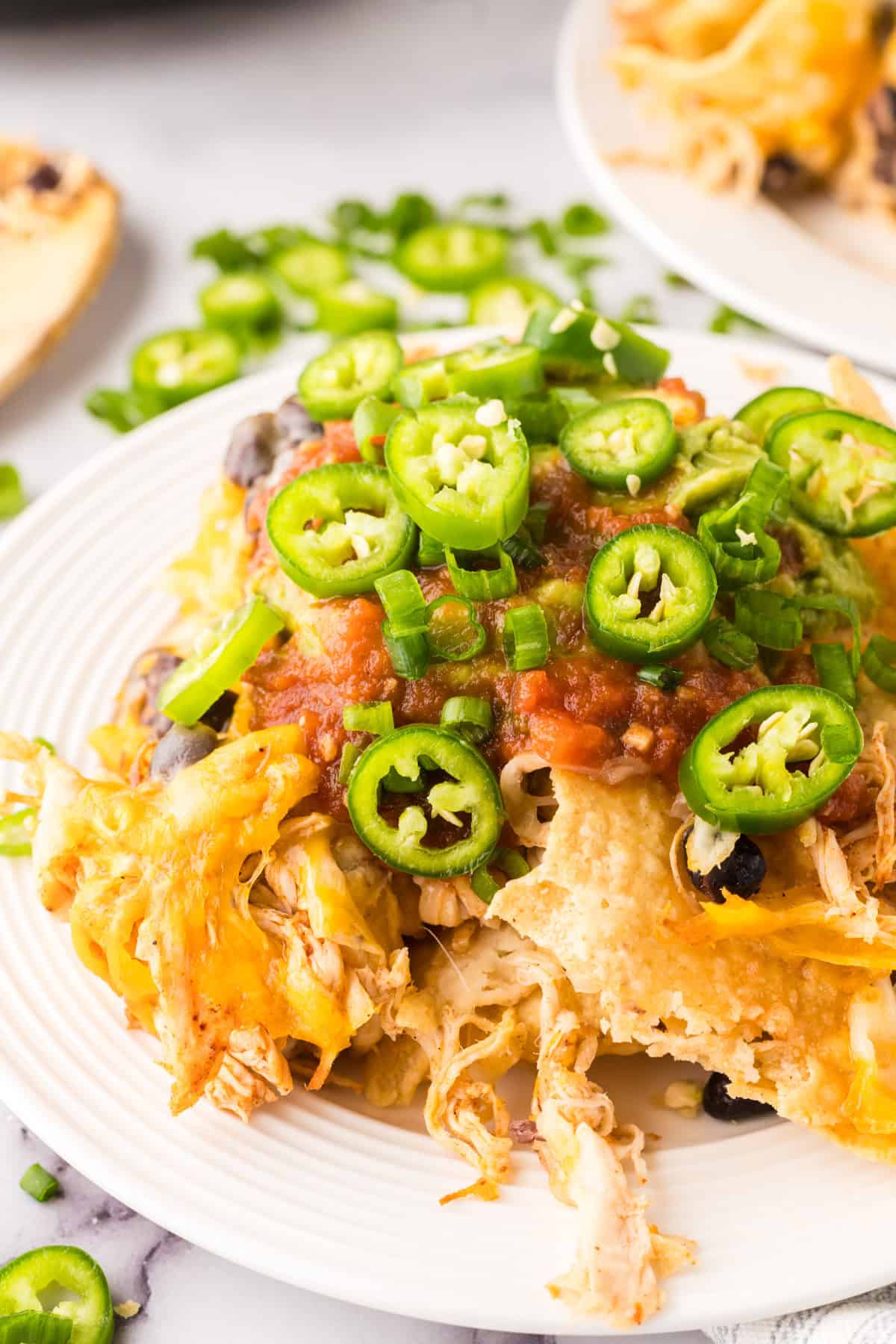 a round white plate with skillet, shredded chicken nachos with melted cheese and jalapeños on top.