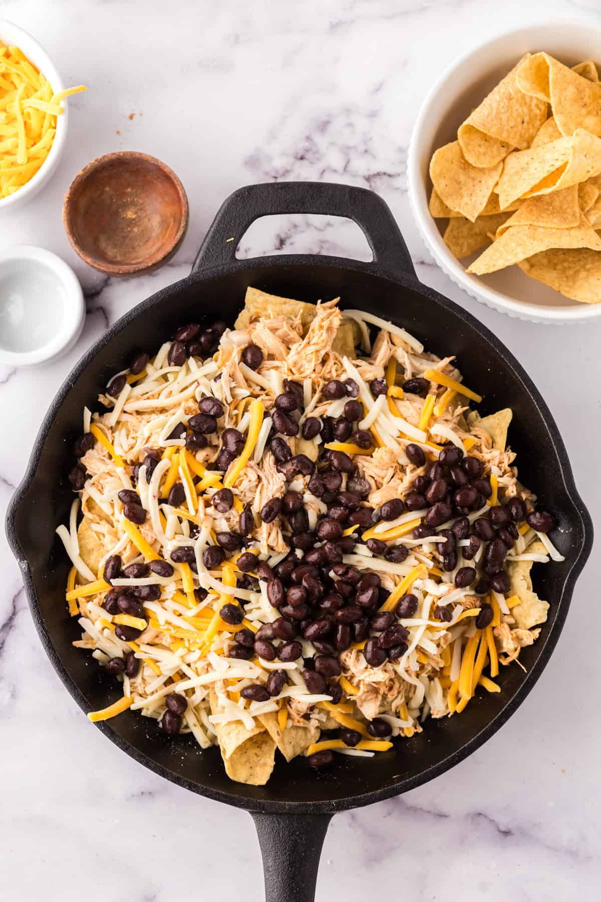 cast iron skillet with chips, chicken, and other ingredients for the skillet chicken nachos.