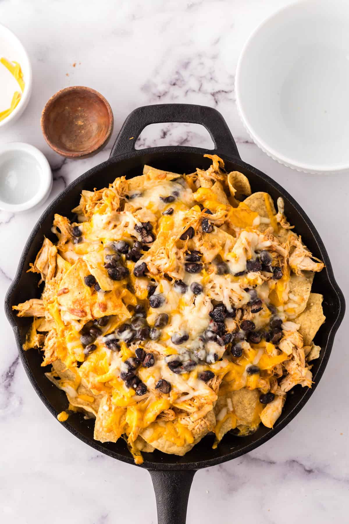 cast iron skillet with chips, chicken, and other ingredients for the skillet chicken nachos.