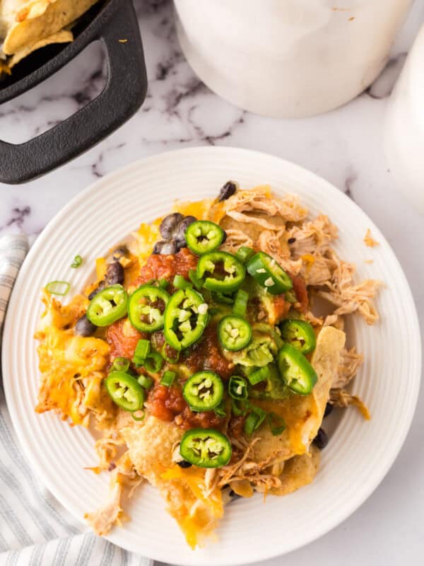 a round white plate with skillet, shredded chicken nachos with melted cheese and jalapeños on top.