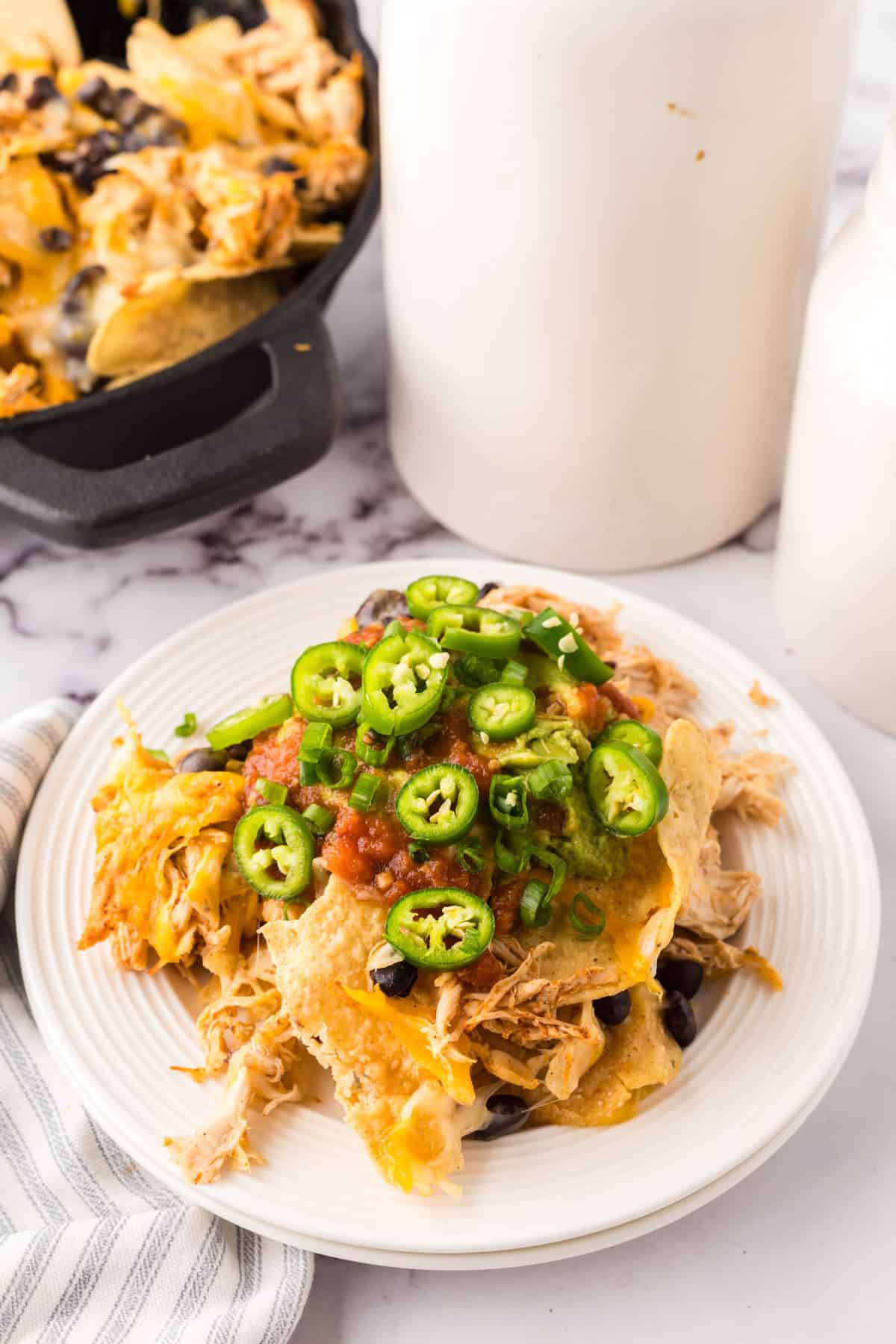 a round white plate with skillet, shredded chicken nachos with melted cheese and jalapeños on top.