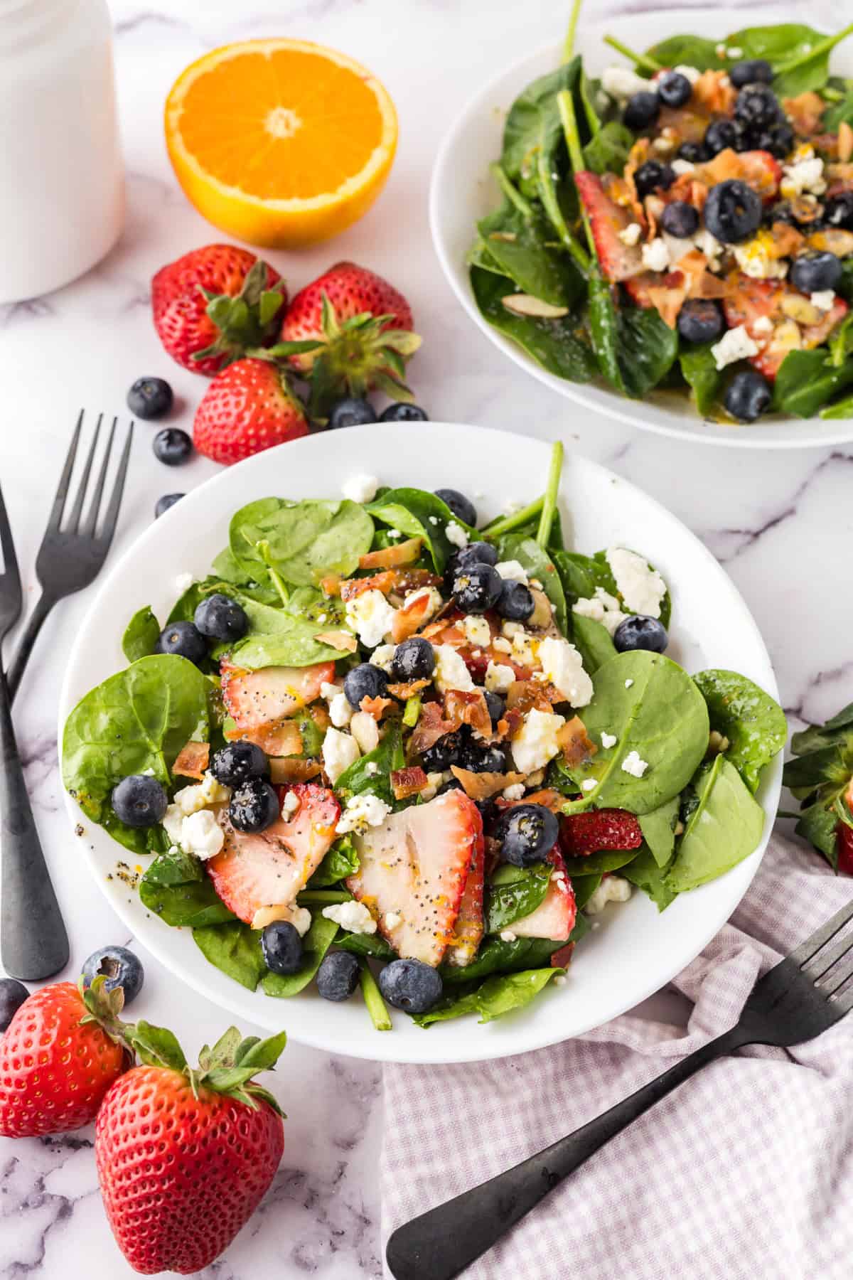 spinach and berry salad on a round white plate with black forks to the side.
