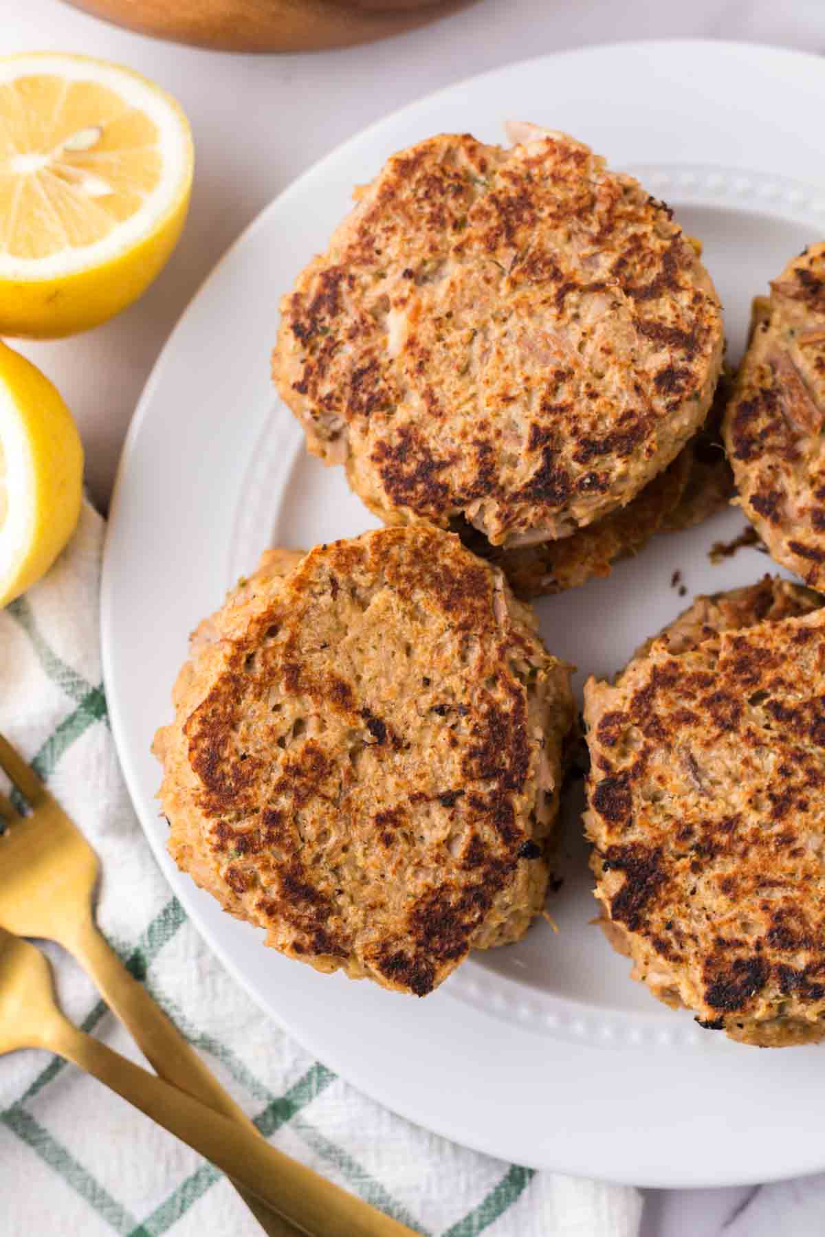 four tuna patties on a round white plate with lemons to the side.