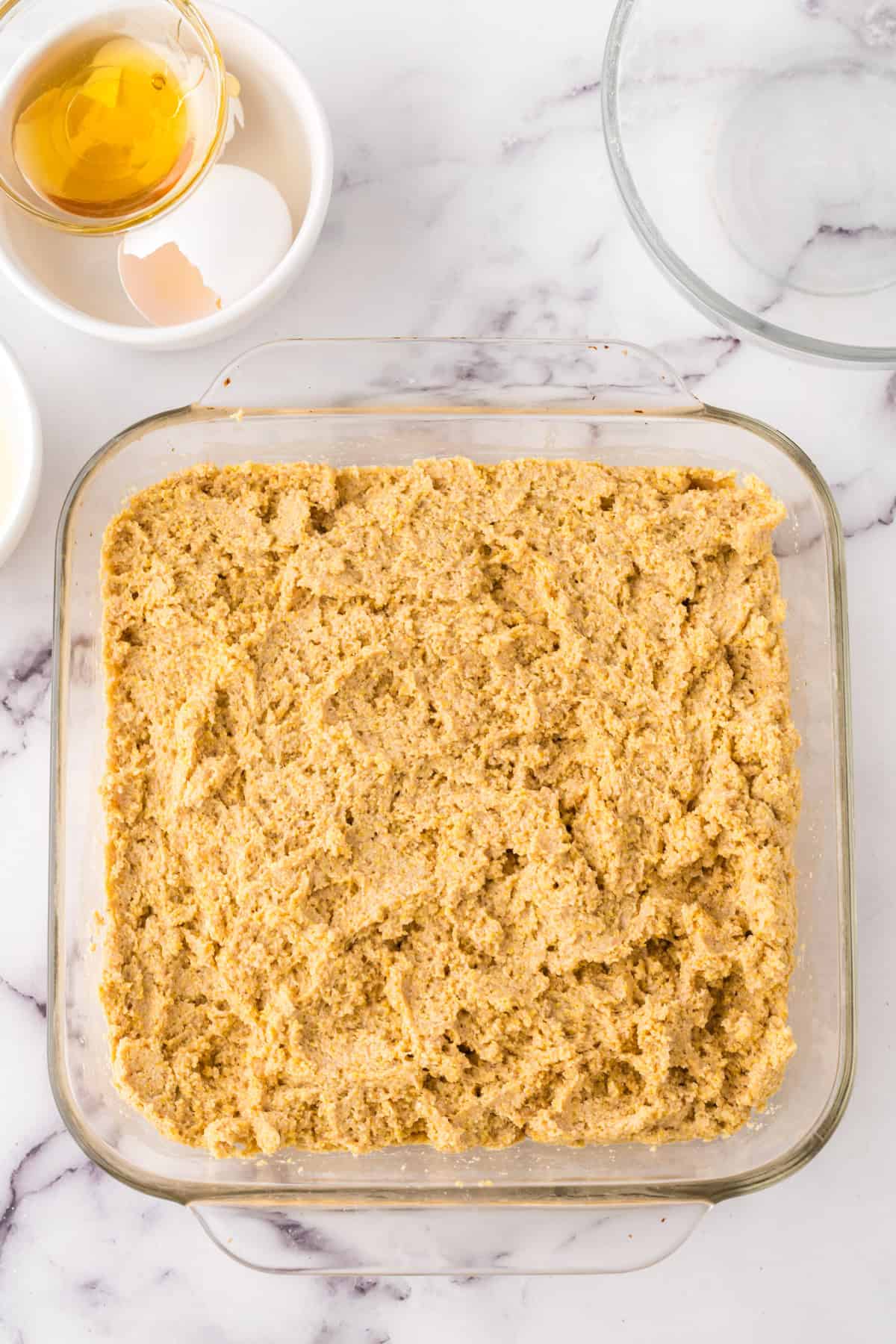 clear baking dish with whole wheat cornbread batter inside ready to bake.