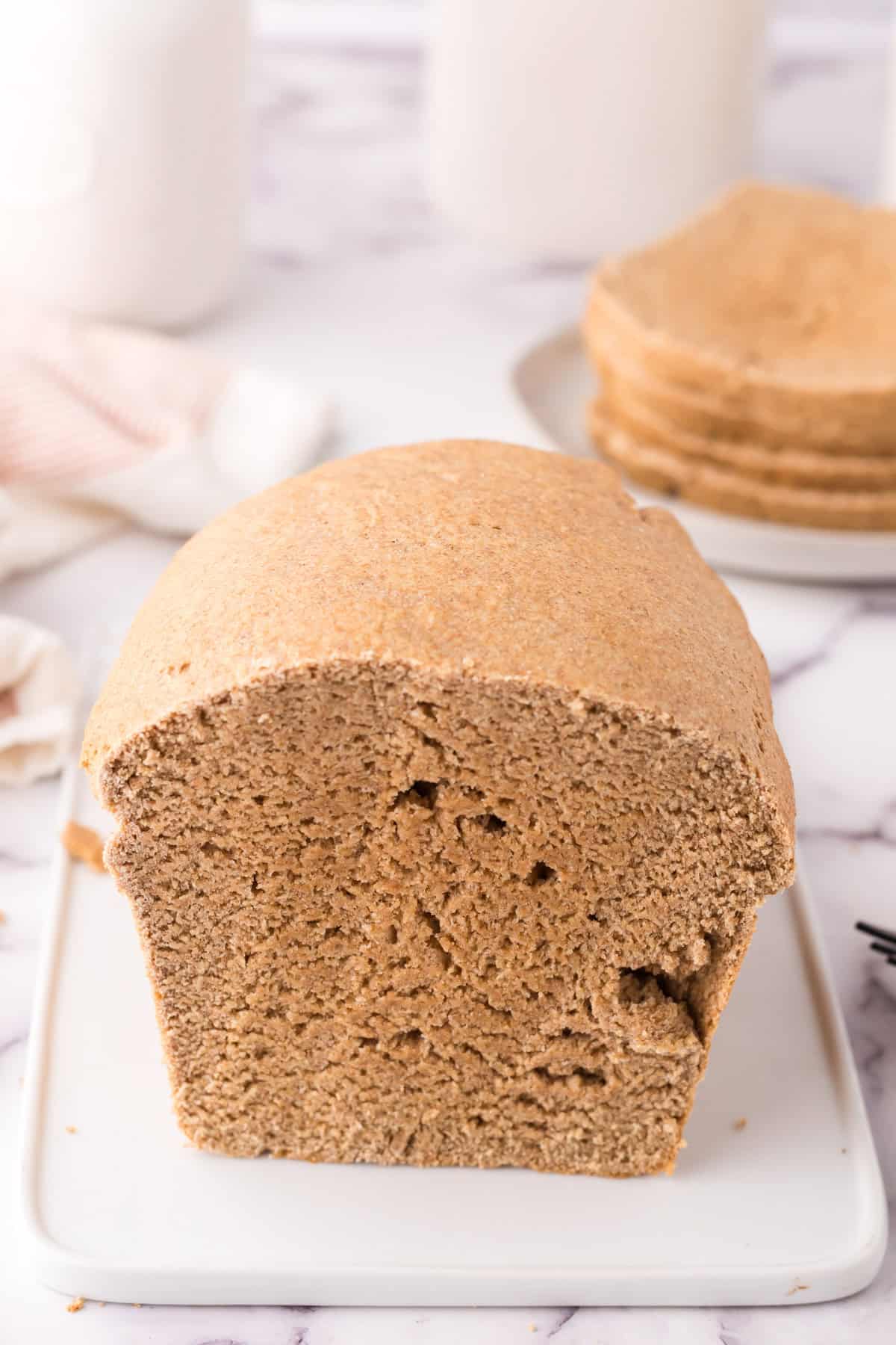 whole wheat sandwich bread recipe slices stacked on a plate behind the sliced loaf.