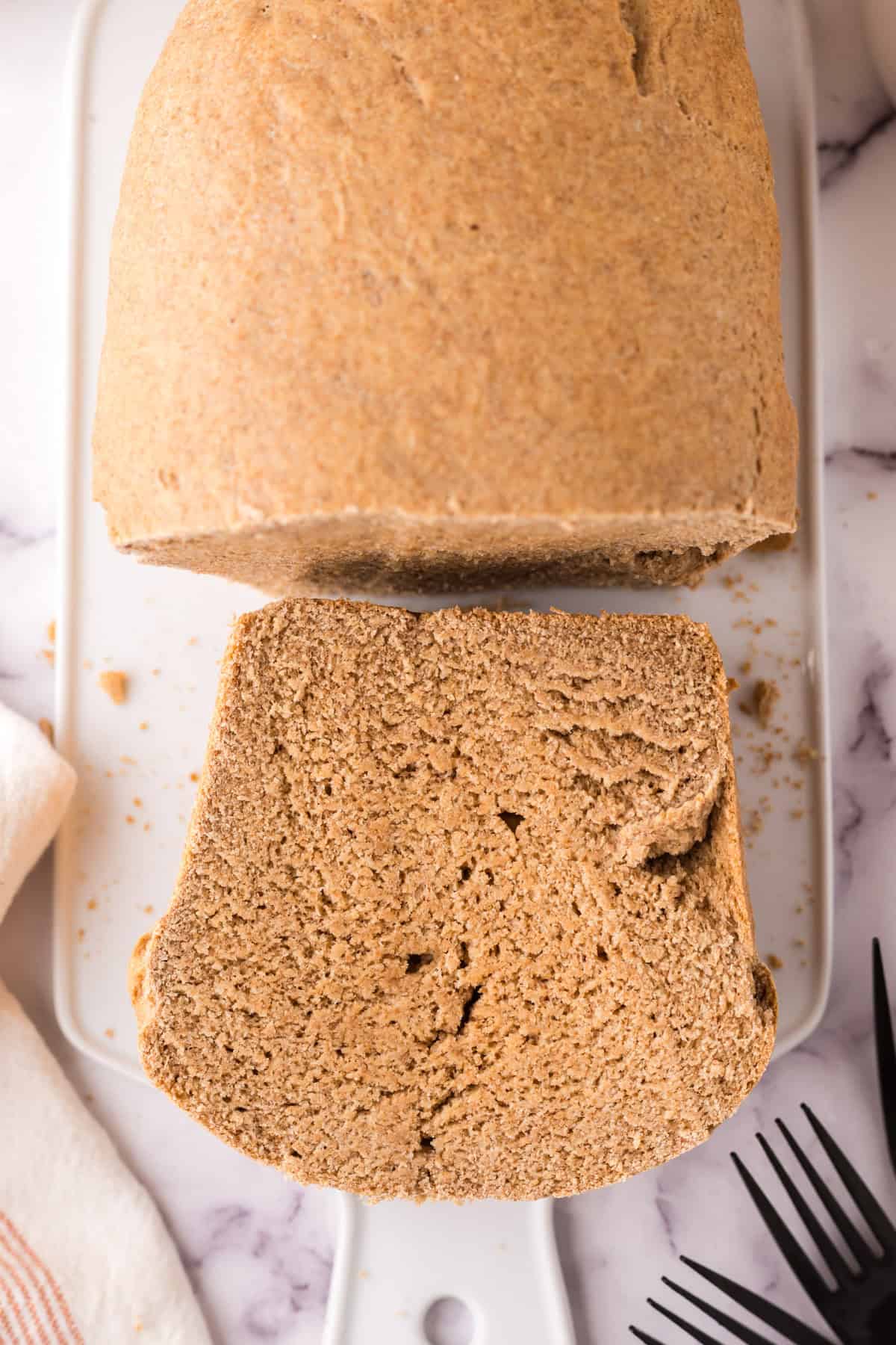 whole wheat sandwich bread recipe slices stacked on the cutting board next to the cut half loaf.