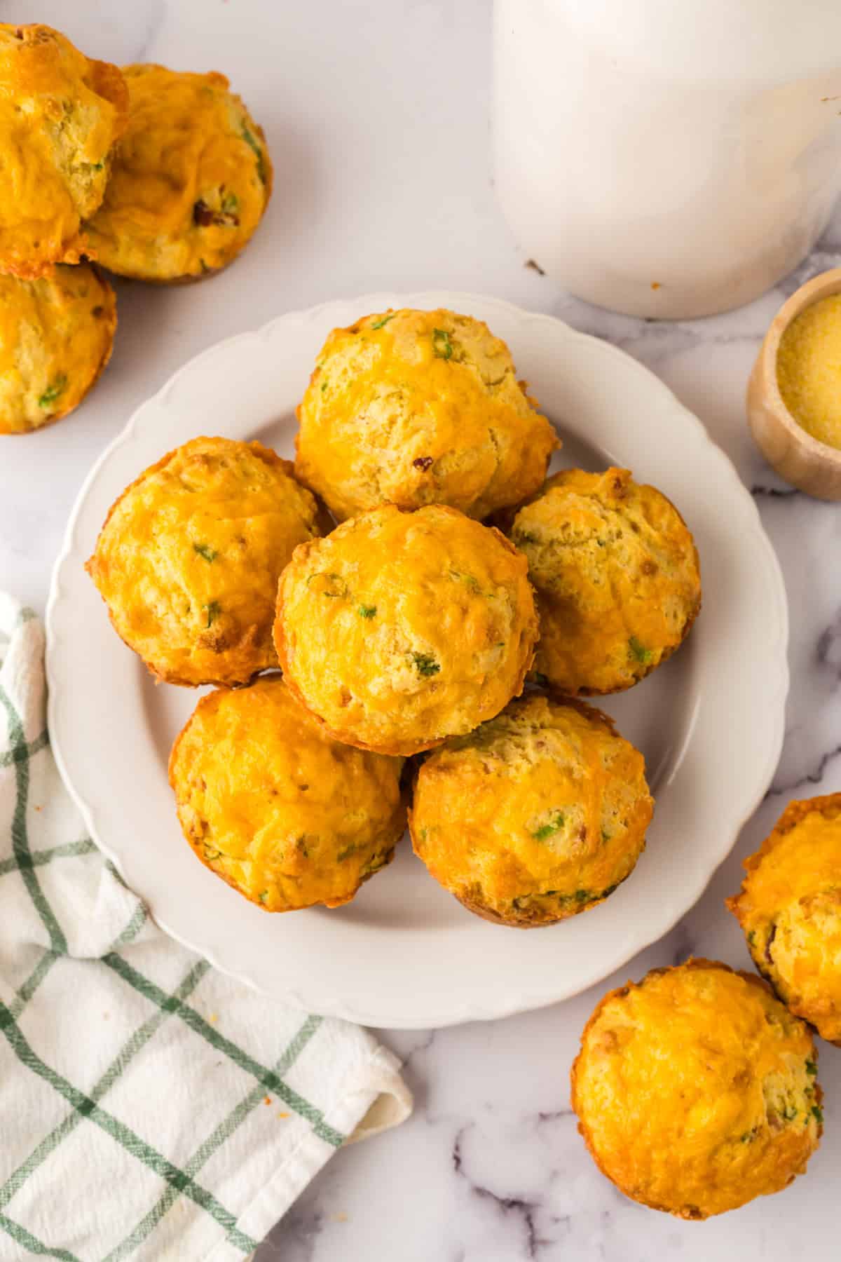 baked cheddar bacon cornbread muffins stacked on a round white plate.