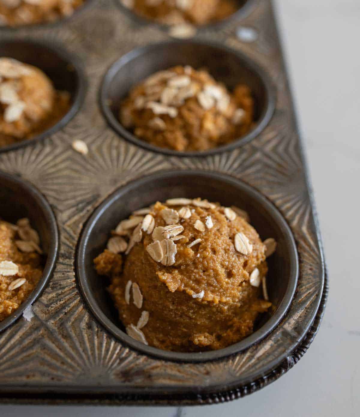 healthy pumpkin muffin dough into the tin with oats on top.