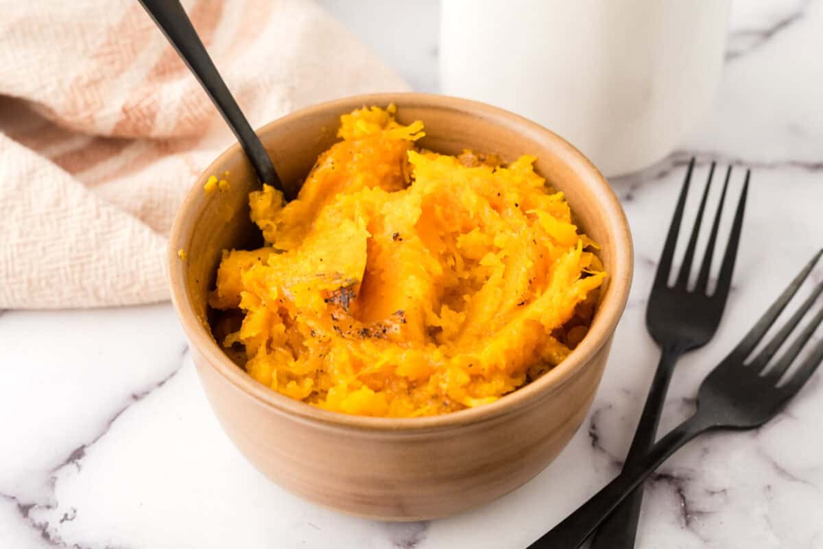 baked soft and smashed butternut squash in a small bowl with a black fork.