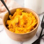 baked soft and smashed butternut squash in a small bowl with a black fork.