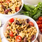 two white bowls of Italian Pasta Salad Recipe with whole cherry tomatoes and golden spoons to the side.