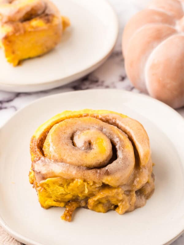 pumpkin cinnamon rolls on round white plates.