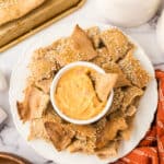simple lavish bread crackers on a round plate with a bowl of dip in the middle.
