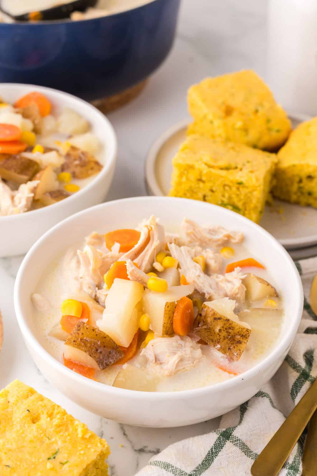 two white serving bowls of baked potato corn chowder next to zucchini cornbread.