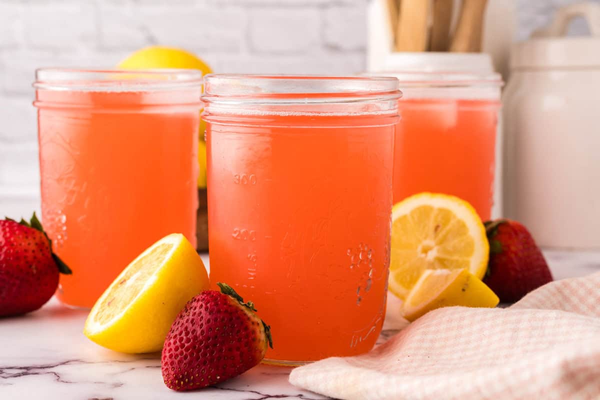 mason jars filled with fresh strawberry rhubarb lemonade with lemons al around.