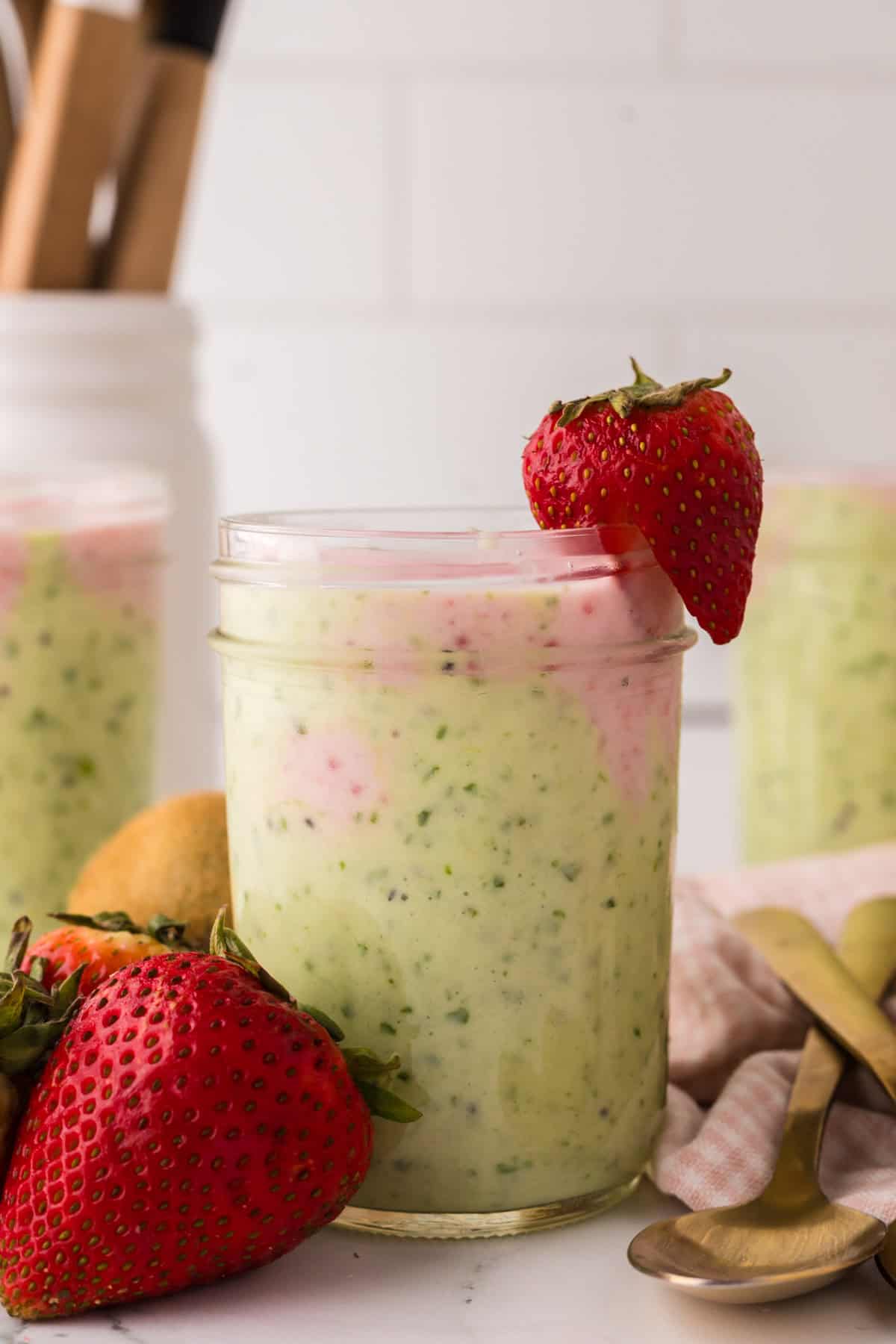 mason jar with strawberry kiwi smoothies inside and a strawberry on top.