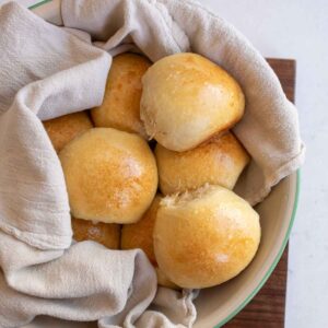 golden brown baked rolls in blue and white bowl with white towel.
