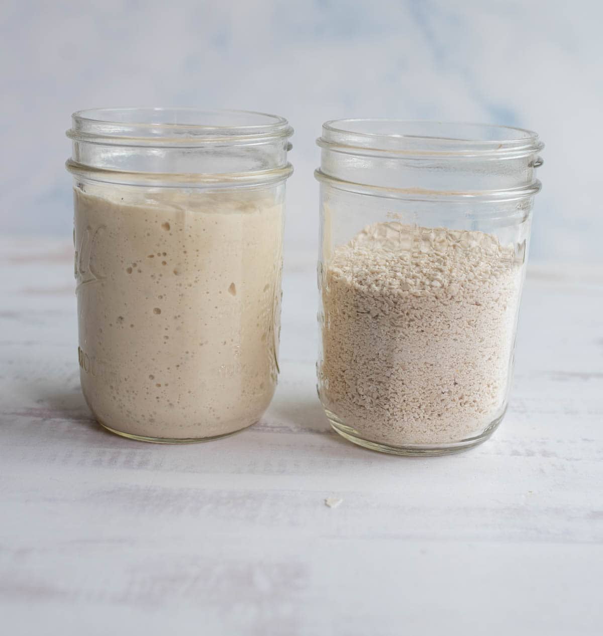 a jar of active bubbly sourdough starter sitting next to a jar of dehydrated starter crumbs.