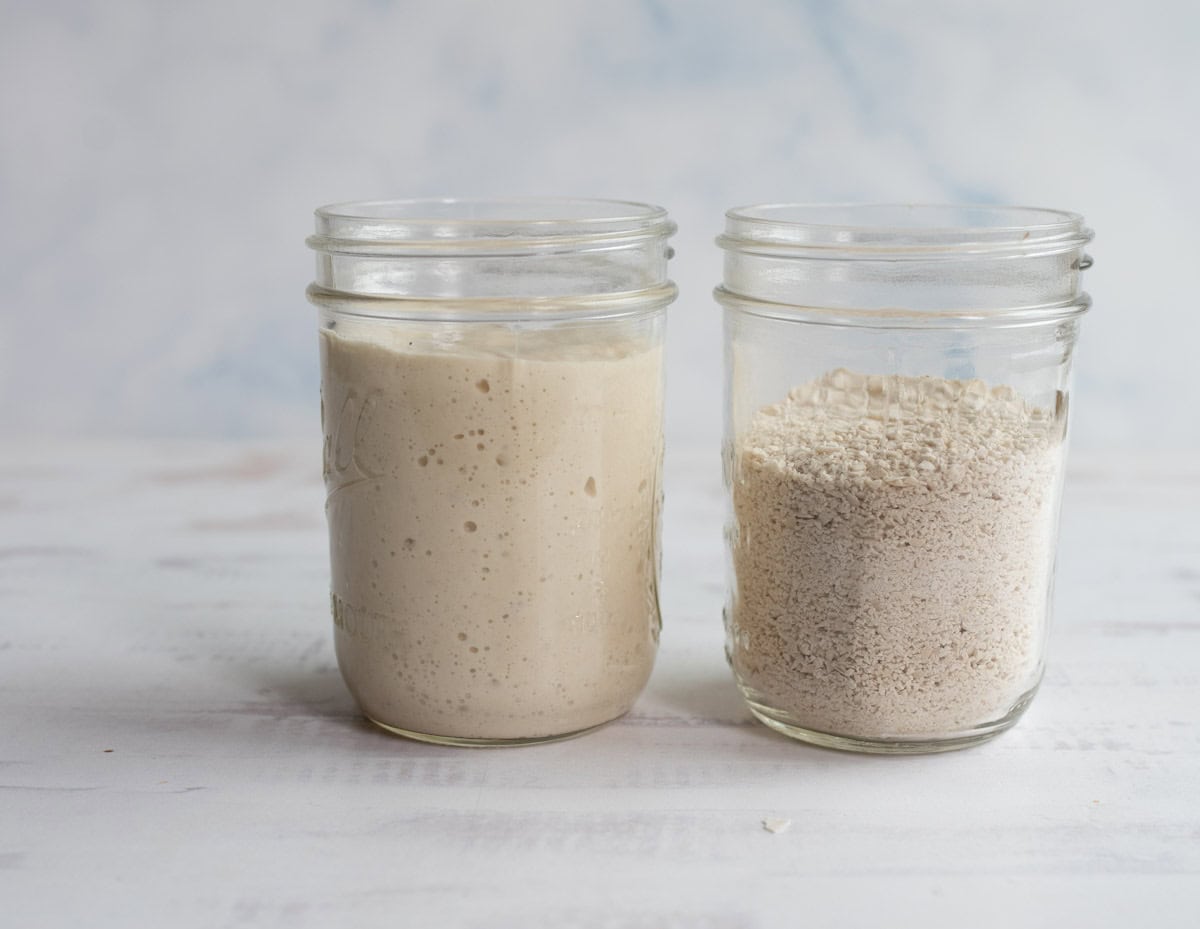 Two glass jars on a light surface; the left jar contains bubbly, active sourdough starter showing how to rehydrate sourdough starter, while the right jar holds dry starter. Both jars are about two-thirds full and set against a pale, blurred background.