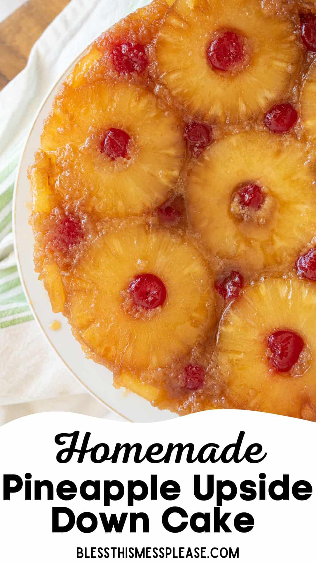 Top view of a homemade pineapple upside down cake with circular pineapple slices and cherries on top. The cake is placed on a white plate, with a green-striped cloth partially visible underneath. Text at the bottom says Homemade Pineapple Upside Down Cake.