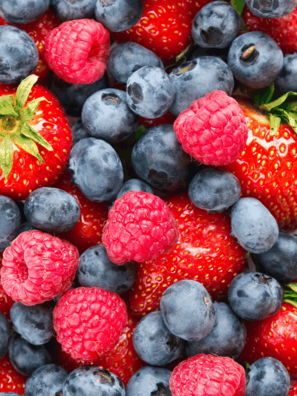 A close-up view of fresh strawberries, blueberries, and raspberries, showing their vibrant red and blue colors. The berries are mixed together, filling the entire frame—perfect for learning how to preserve berries at their freshest.