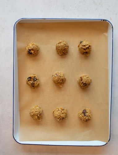 A baking tray lined with parchment paper holds nine evenly spaced scoops of unbaked cookie dough, arranged in a 3x3 grid pattern.