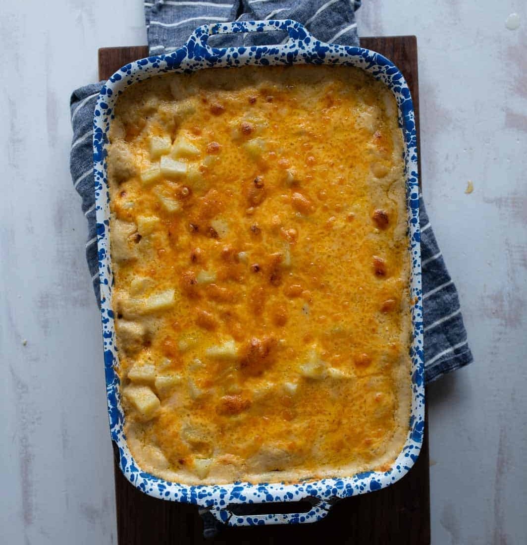 A blue and white speckled baking dish filled with cheesy, golden-brown scalloped potatoes sits on a striped kitchen towel and wooden board.