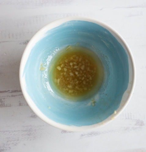 A blue and white bowl with minced garlic and liquid, likely a marinade or dressing, on a white surface.
