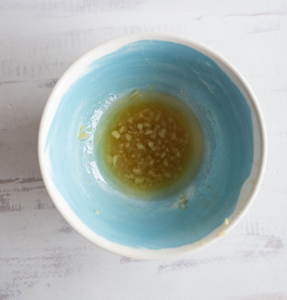 A blue and white bowl with minced garlic and liquid, likely a marinade or dressing, on a white surface.