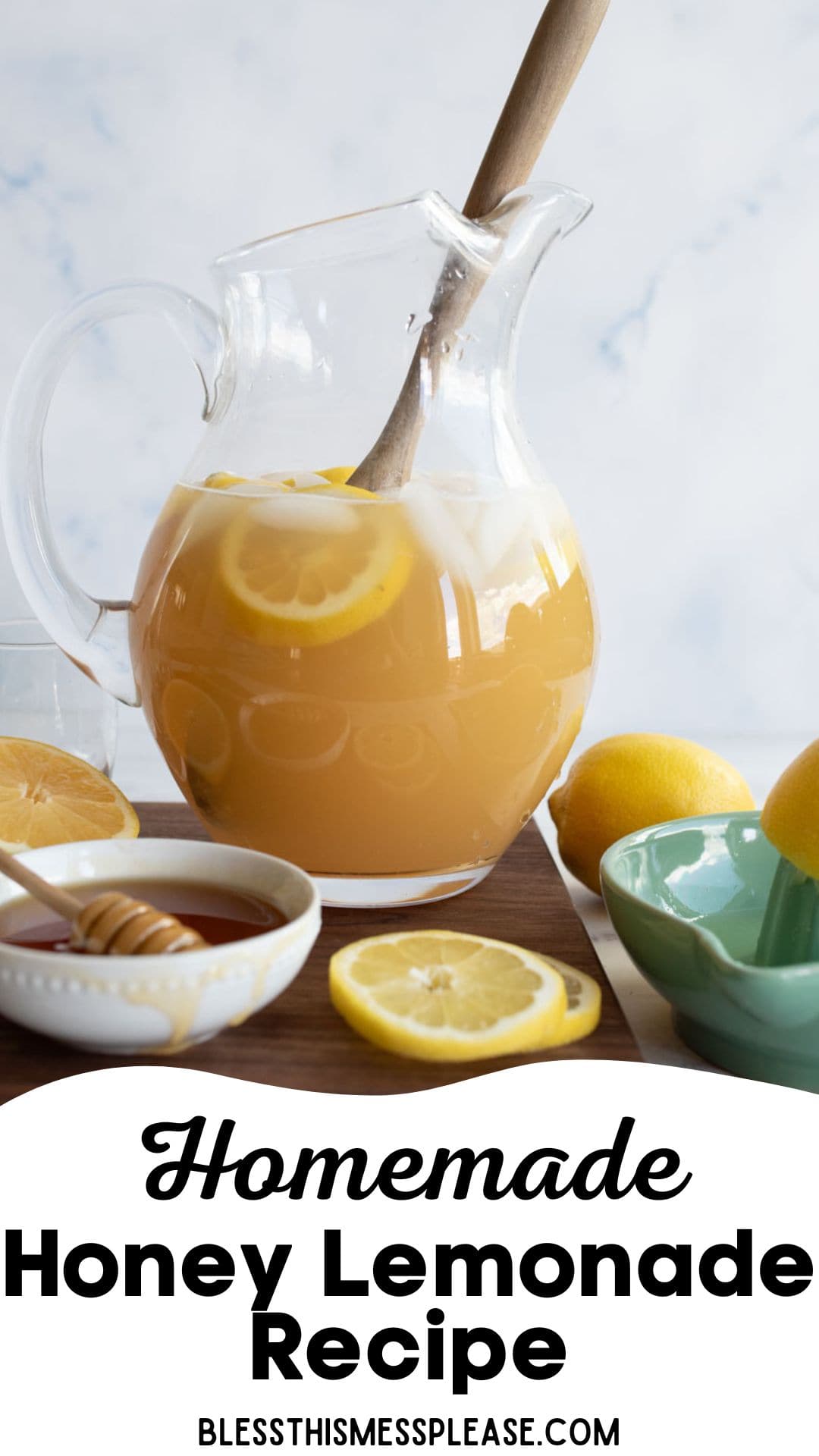A glass pitcher filled with honey lemonade, lemon slices, and a wooden spoon is on a table with fresh lemons, a bowl of honey with a dipper, a glass, and part of a teal bowl. Text reads Homemade Honey Lemonade Recipe.