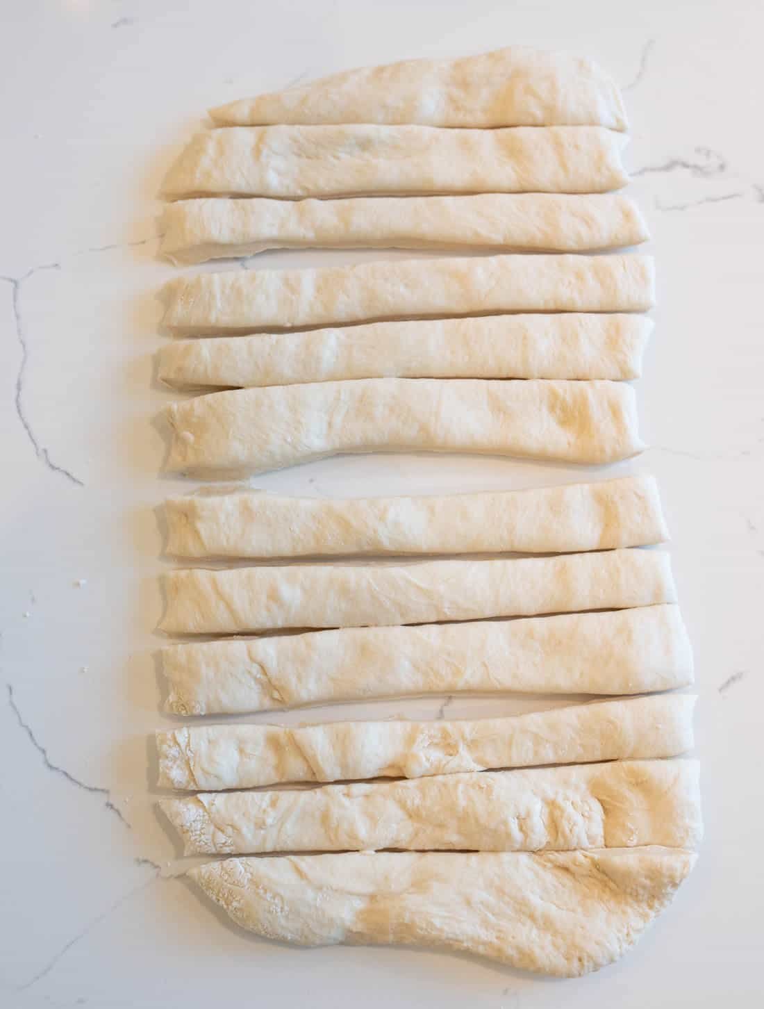 Rectangular dough on a white surface, cut into evenly sized strips ready for baking or cooking.