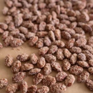 A close-up view of many sugar-coated roasted almonds, crafted using a classic candied almonds recipe, spread out on a sheet of brown parchment paper.