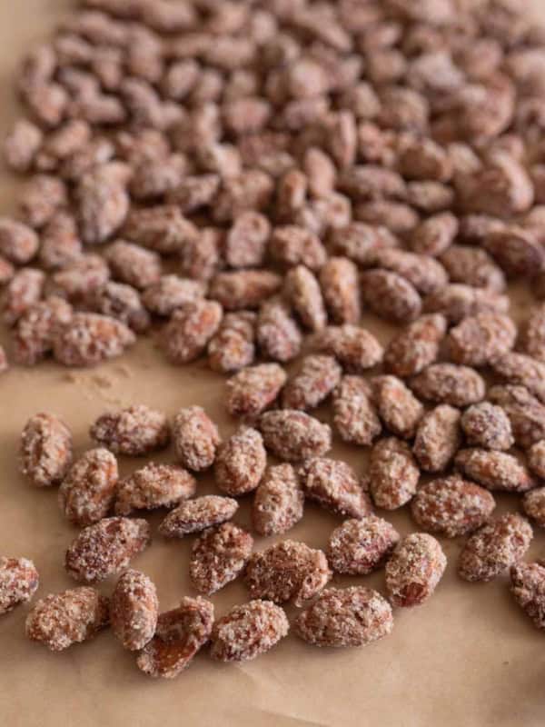 A close-up view of many sugar-coated roasted almonds, crafted using a classic candied almonds recipe, spread out on a sheet of brown parchment paper.