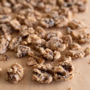 Close-up of clusters of walnuts, coated in a layer of sugar and spices, scattered on a sheet of brown parchment paper from a candied walnuts recipe.