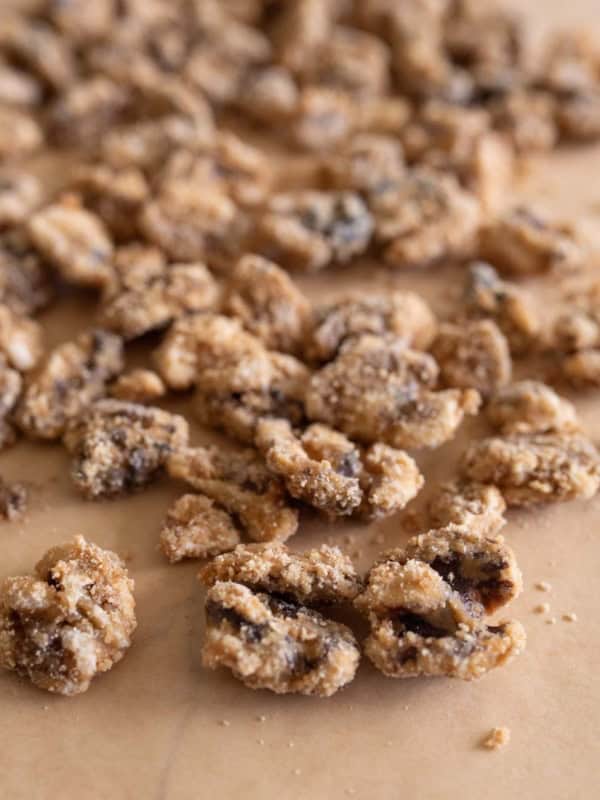 Close-up of clusters of walnuts, coated in a layer of sugar and spices, scattered on a sheet of brown parchment paper from a candied walnuts recipe.