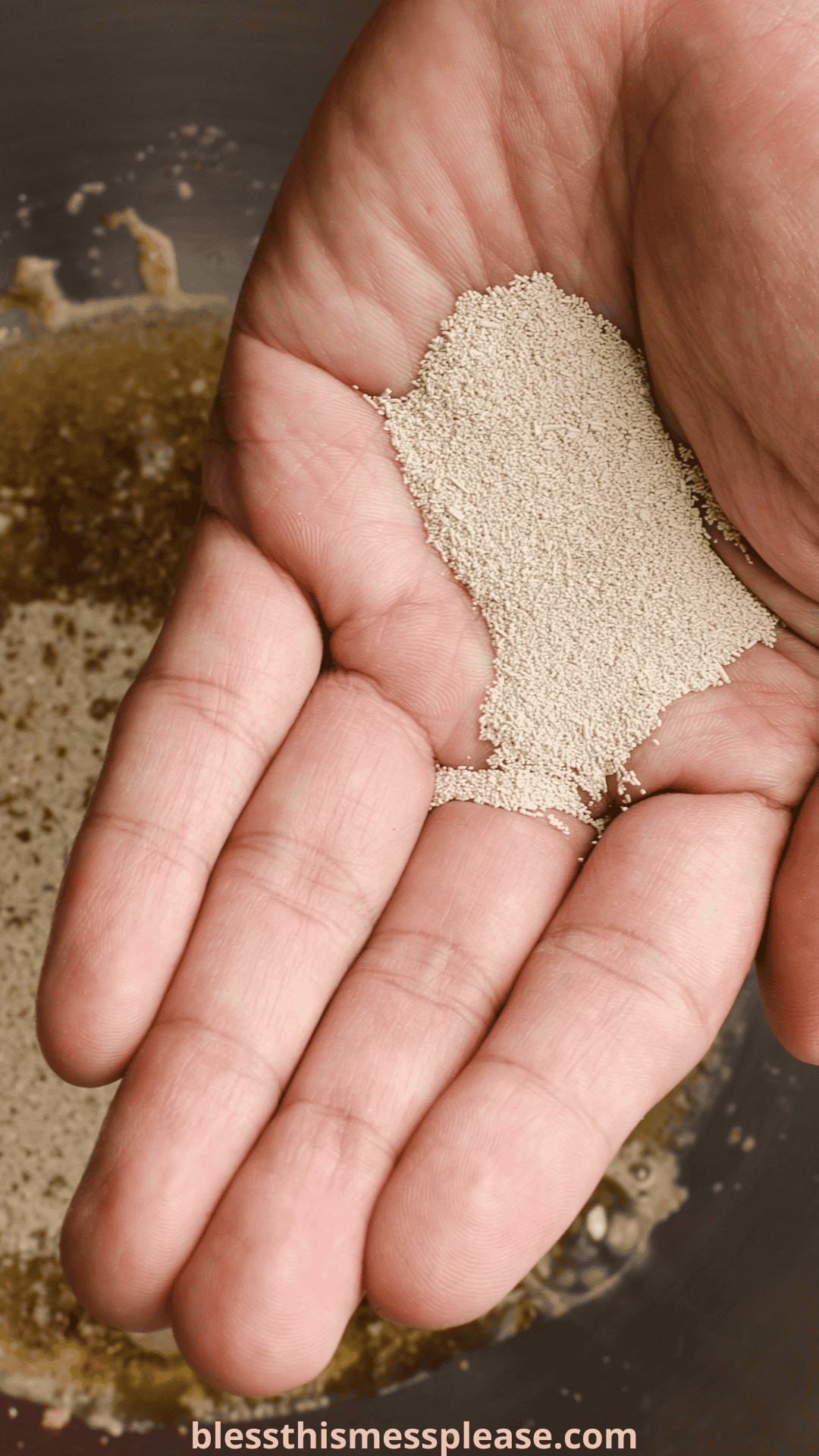 A close-up of a hand holding dry active yeast over a mixing bowl with liquid ingredients, illustrating the step where bakers often consider instant yeast vs active dry yeast for their recipes.