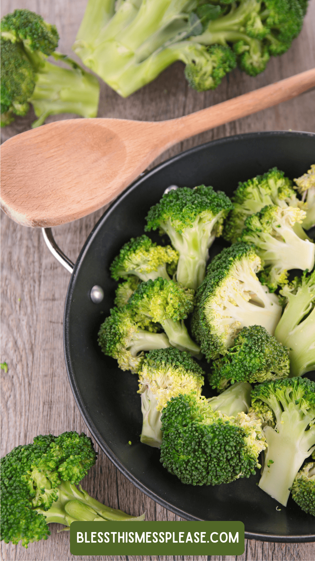 A frying pan filled with fresh broccoli florets sits on a wooden surface next to a wooden spoon, with more broccoli for how to preserve broccoli and a website label blessthismessplease.com visible.