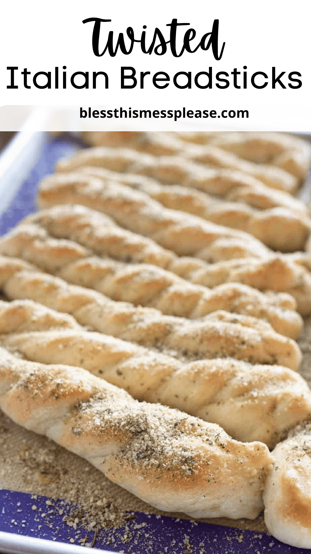A tray of freshly baked Italian breadsticks, twisted and sprinkled with herbs and seasoning, arranged in neat rows on a baking sheet.