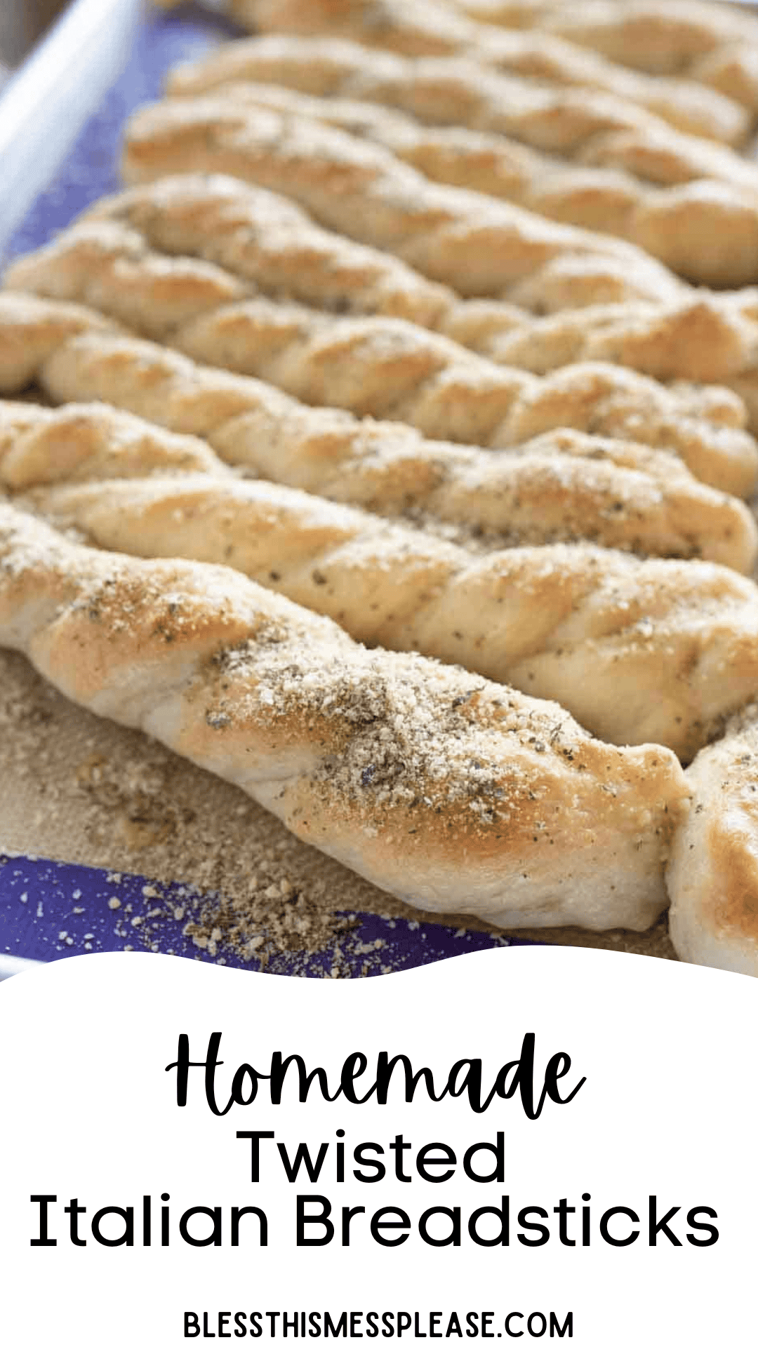 A tray of freshly baked, twisted Italian breadsticks sprinkled with herbs and seasoning rests on a baking sheet. Text on the image reads: Homemade Italian Breadsticks. blessthismessplease.com.