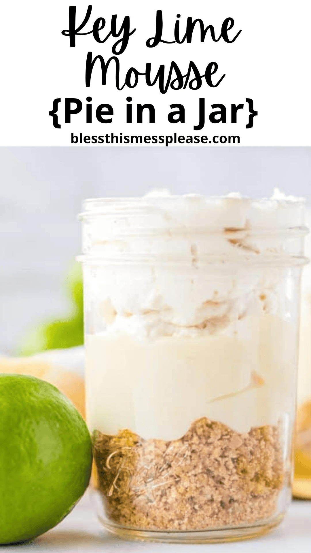 A mason jar filled with creamy key lime mousse and graham cracker crumbs sits on a white surface, with a fresh lime beside it. The text above reads, Key Lime Mousse {Pie in a Jar} blessthismessplease.com.