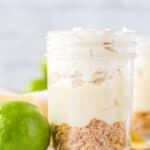 A mason jar filled with key lime mousse featuring a crumbly graham cracker crust, creamy filling, and whipped topping, with a fresh lime placed beside the jar.
